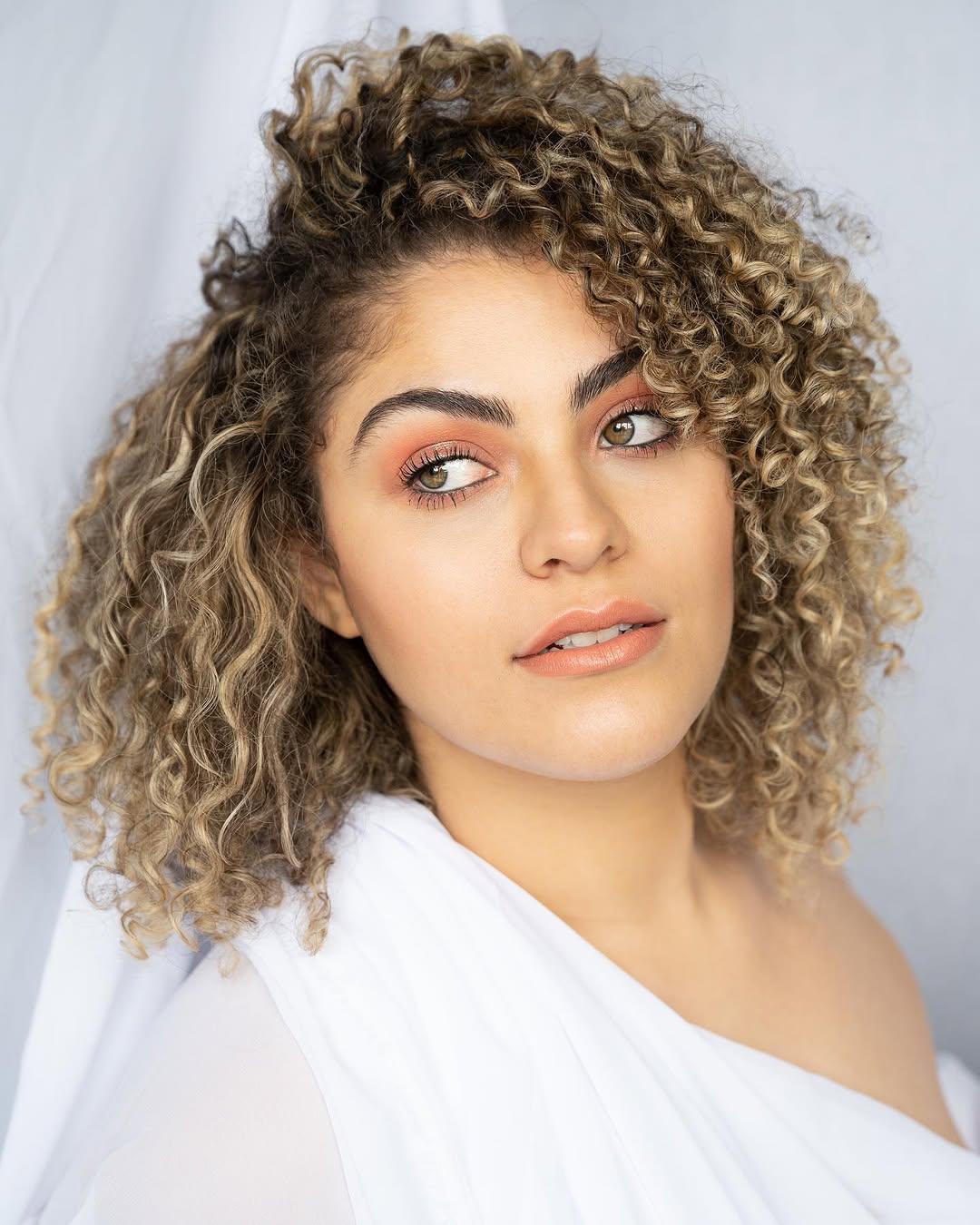 Frisse make-up met zachte perzikkleurige oogschaduw en natuurlijke krullen