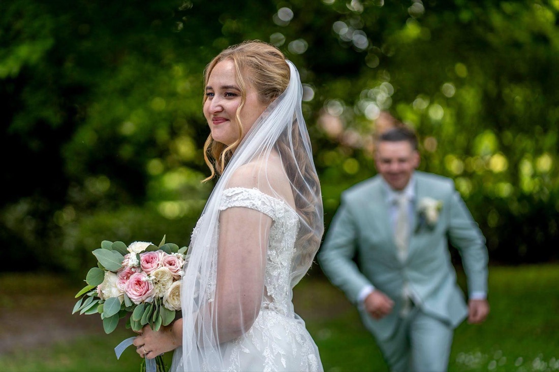 Cheryl met bruidsboeket en sluier, haar bruidegom op de achtergrond