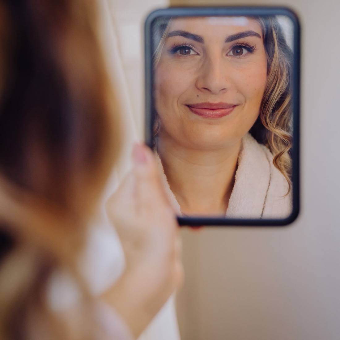 Bruid bekijkt haar zachte, natuurlijke make-up in een handspiegel